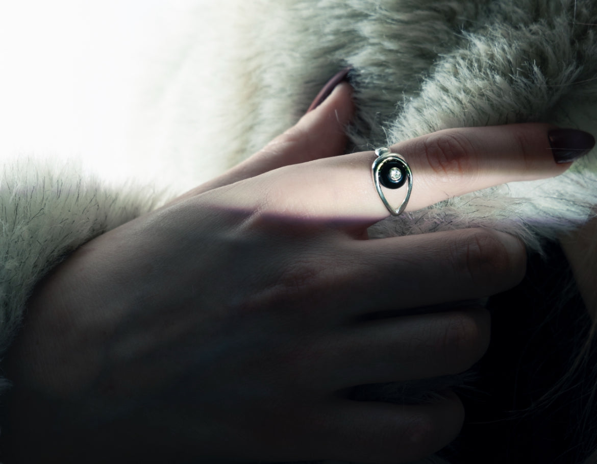 Hand wearing a silver Tally Ho ring with a black onyx stone and white topaz on a textured surface
